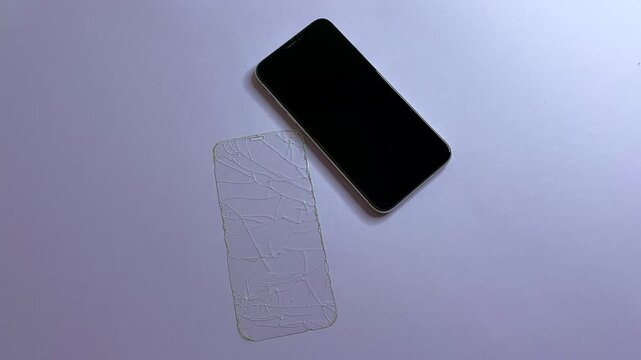 A removed protective glass next to an undamaged smartphone on mono bright background