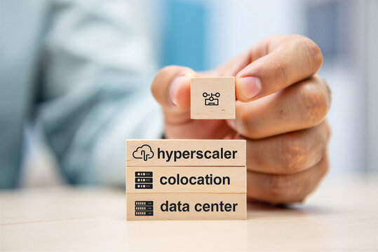 Hand holding wooden block with network diagram icon above stack of blocks illustrating hyperscaler collocation data center concepts