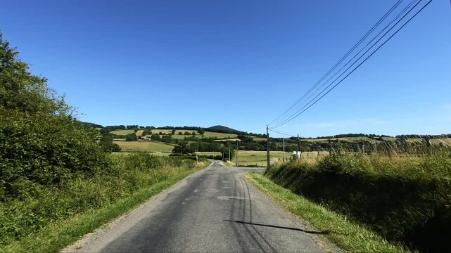 Scenic country road winding through green fields and rolling hills under a clear blue sky in the Morvan region of France.