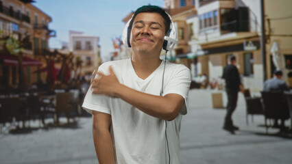 Man wearing white headphones and white t shirt crosses arms hugging chest on a sunny european...