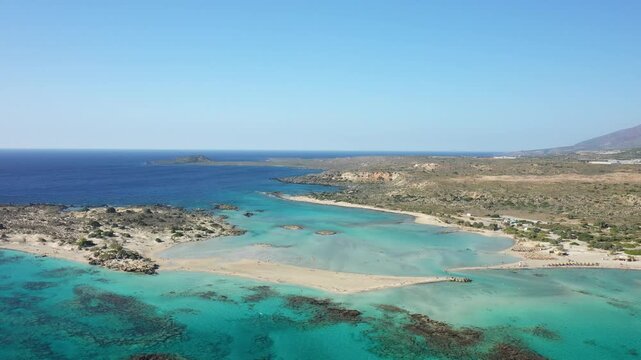 Stunning aerial view of Elafonisi beach with turquoise waters and sandy shores on the island of Crete, Greece. The landscape features clear blue sea, rocky coastline, and natural beauty under a clear