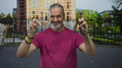 Obraz premium Man with hoary long hair makes air quotes with both hands on a city street by a building in daylight; sarcasm irony.