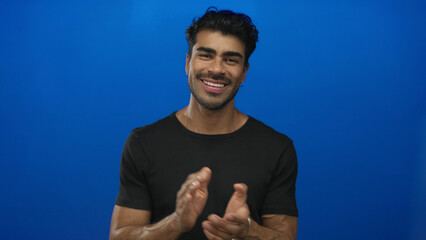 Fototapeta premium Man clapping hands energetically and smiling with open posture in bright blue studio environment; joy celebration.