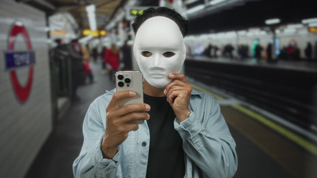 Man holding white mask near his face while gripping smartphone at train station platform building; anonymity.
