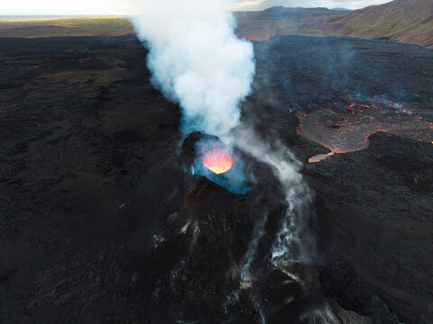 Aerial view of the fiery heart of the volcano spewing smoke and lava against the stark, black landscape, Grindavik, Iceland.