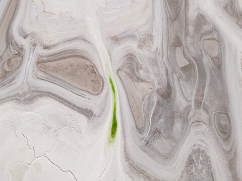 Aerial view of swirling patterns of white and grey earth, accented by a vibrant streak of green, Old Chandler Potash Mine Site, Western Australia, Australia.