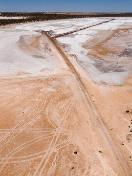 Aerial view of stark white salt flats meeting the rusty, textured earth under a clear blue sky at the Old Chandler Potash Mine Site, Western Australia, Australia.