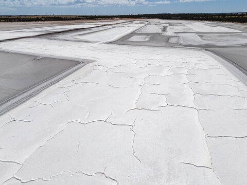 Aerial view of stark white salt flats stretch across the landscape, cracked and textured under the harsh sun, Old Chandler Potash Mine Site, Western Australia, Australia.