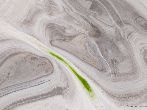 Aerial view of swirling white and grey earth, punctuated by a vibrant green channel, Old Chandler Potash Mine Site, Western Australia, Australia.