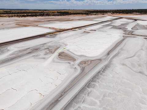 Aerial view of shimmering white salt flats, cracked earth textures, and contrasting dark pathways stretch across the landscape, Old Chandler Potash Mine Site, Western Australia, Australia.