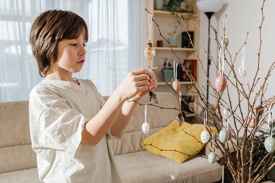 Boy decorating colorful Easter eggs on branches at home