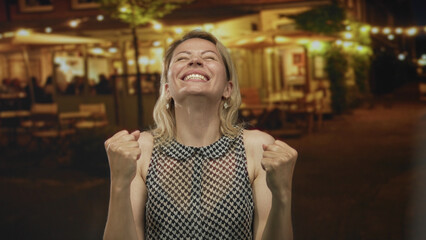 Fototapeta premium Woman with raised arms and clenched fists in hotel building interior amid warm lighting; joy victory moment.
