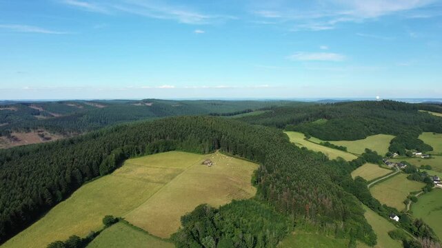 Scenic aerial view of rolling hills, forests, and fields in the Morvan countryside under a clear blue sky. Lush greenery and rural farmland create a tranquil natural scene.