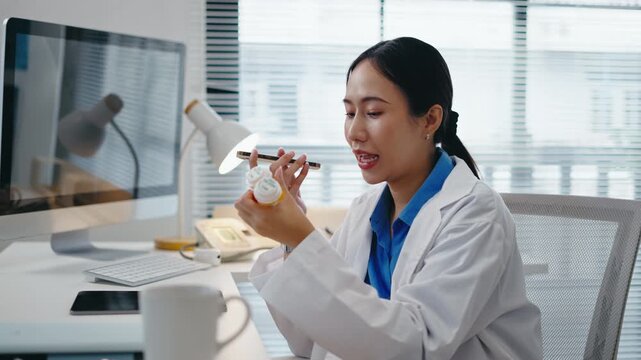Asian female doctor using AI chatbot,virtual assistant,Ai voice command on smartphone to check prescription pills in a modern hospital office.Concept of telemedicine,health tech and digital healthcare