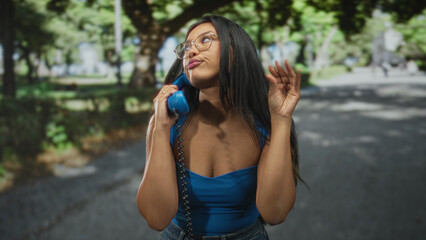 Naklejka premium Young hispanic woman holding vintage telephone handset to ear while making a dismissive hand gesture on a street; sassy attitude.