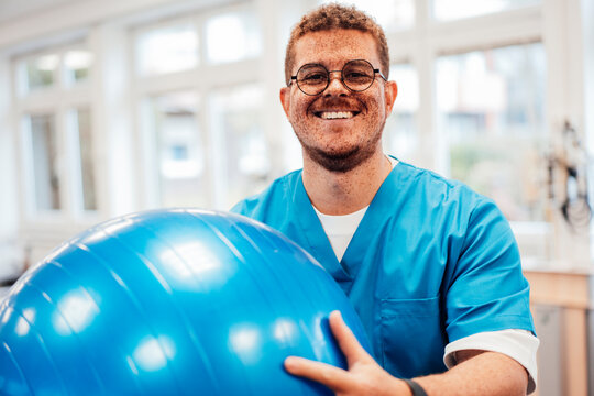 Smiling physiotherapist indoors with exercise ball in physiotherapy setting