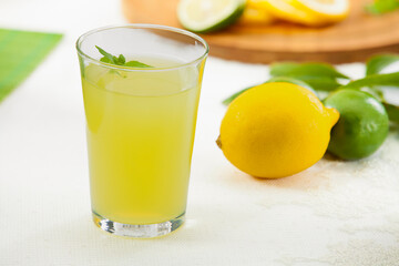 Fresh homemade lemonade or lime juice in a glass with lemon and lime slices on a wooden board, bright garden background.