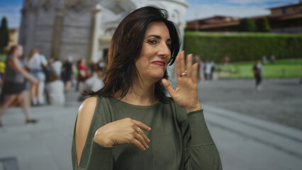Fototapeta premium Woman with bare chin touches face at leaning tower building in crowded tourist plaza; contemplation.