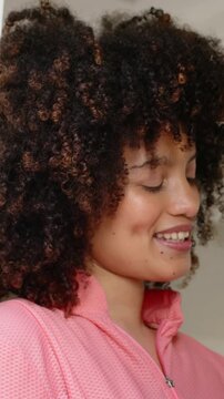 Vertical video: Camera pulling back, woman in pink zip-up tilting head up near doorway, reflecting