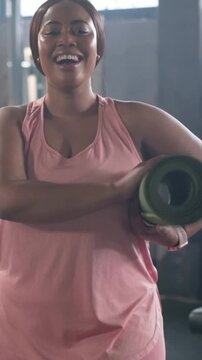 Vertical video: Walking into frame woman in pink adjusting green yoga mat at gym, preparing workout