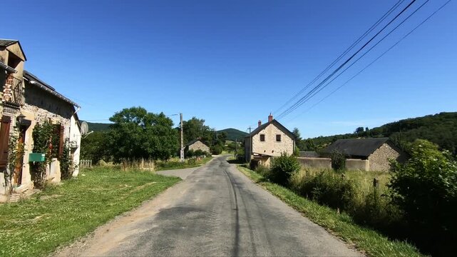 Sunny summer day on a quiet rural road lined with stone houses and green fields in the Morvan region of France. Rolling hills and clear blue sky create a peaceful countryside atmosphere.