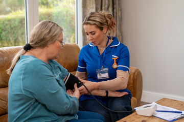 Nurse checks blood pressure of patient in home setting during daytime