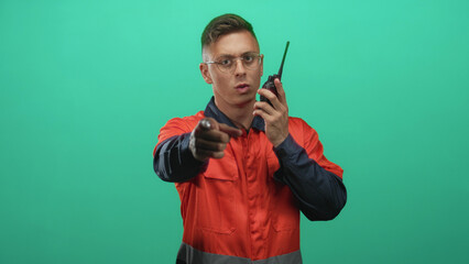 Man mechanic young blond handsome in orange coveralls points finger while holding a radio walkie...