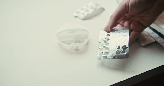 Close up of person placing tablets into weekly pill organizer at home. Suitable for chronic illness management, senior care, and daily health routine themes.