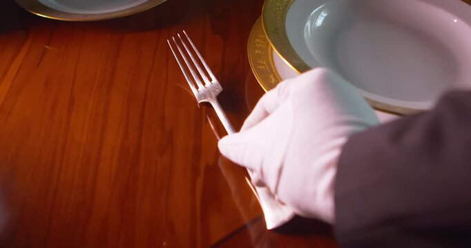 Close up of gloved hand placing utensil beside gold rimmed soup bowl on formal dining table. Suitable for fine dining, luxury hospitality, and premium restaurant service themes.