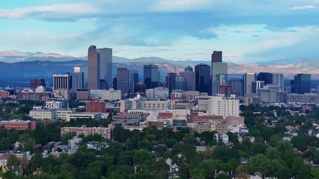 Downtown Denver high rises framed by trees and distant peaks, push in aerial approach