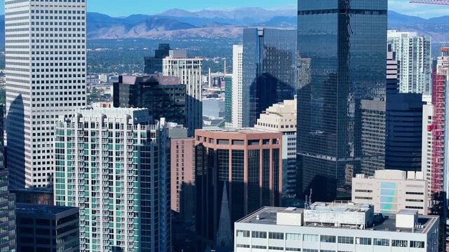 Drone establishing of Denver office towers in bright daylight, tilt up to mountain range, Colorado USA