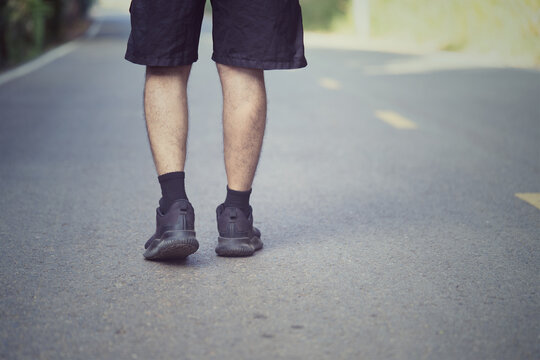 Back view of male runner legs walking on asphalt road during outdoor workout.