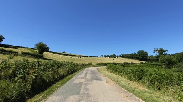 Curving rural road passing through green fields and hay bales under a clear blue sky in the Morvan region of France.