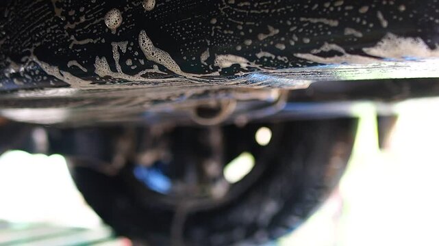 Car underbody washing with soap foam. Hand cleaning vehicle's underside during car wash service.
