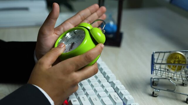 Green alarm clock held over keyboard, Hands holding a small green alarm clock over a white keyboard on a desk
