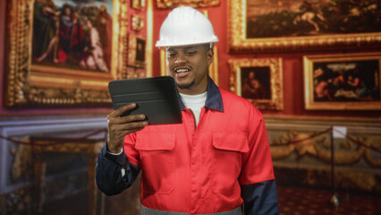 Man construction worker in hard hat and red uniform holding tablet and checking screen in museum gallery  inspection duty. © Krakenimages.com