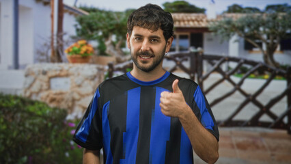 Young hispanic man with beard and earring wearing blue and black football jersey, smiling and...