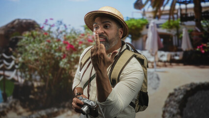 Fototapeta premium Man with backpack holding a vintage camera and flipping his middle finger in a building courtyard; defiance travel attitude.