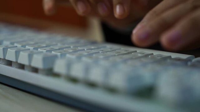Close-up of hands typing on a white computer keyboard, shallow depth of field