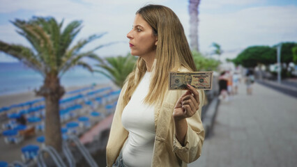Woman holding fifty dollar banknote between fingers on a beachside street, stern gaze and upright posture toward camera  defiance. © Krakenimages.com