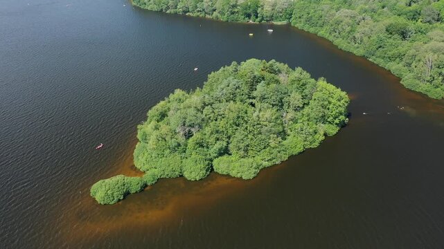 Drone shot of a lush green island surrounded by dark water in Lac des Settons, France. Dense forest vegetation covers the island, creating a vibrant natural scene.
