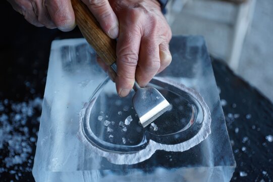 Close-up of skilled hands carving ice sculpture with chisel on block