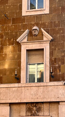 Architectural detail of historic Roman building facade with sculpture and decorative classical elements under blue sky in Rome, Italy.