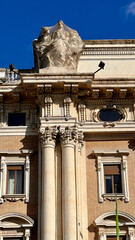 Architectural detail of historic Roman building facade with classical columns and sculptures under blue sky in Rome, Italy.