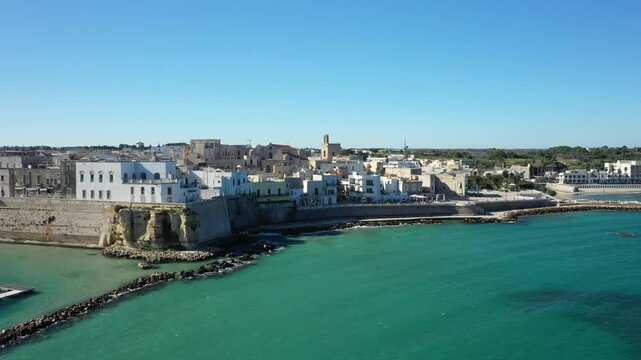 Aerial view of the historic seaside town of Otranto, Italy, featuring turquoise waters and traditional Mediterranean architecture under a clear blue sky.