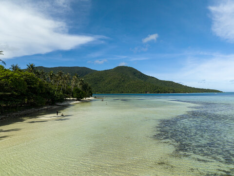 Aerial view of the tranquil turquoise waters meet the sandy shore, framed by lush greenery and distant hills, Bobby Beach, Karimunjawa, Central Java, Indonesia.