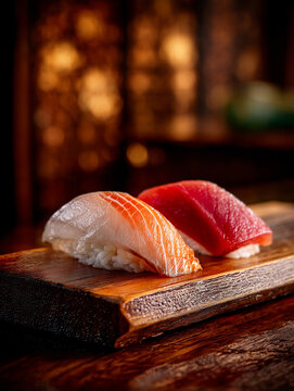 Two pieces of high-quality nigiri sushi, featuring yellowtail (Hamachi) and lean tuna (Akami), served on a traditional dark wood sushi board with bokeh background.