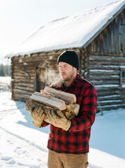 Man carrying firewood while standing in snowy outdoor setting  