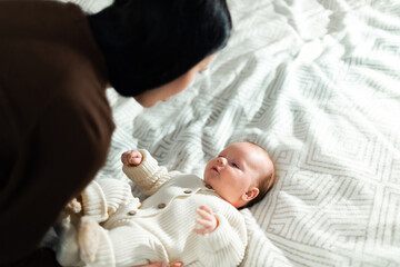 Mother gently holding her newborn baby in a cozy knitted outfit on a patterned blanket