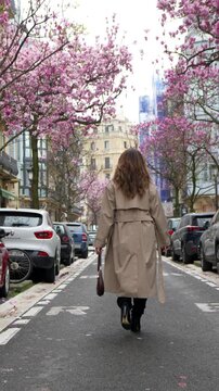 Elegant woman walking down parisian street with blooming magnolia trees